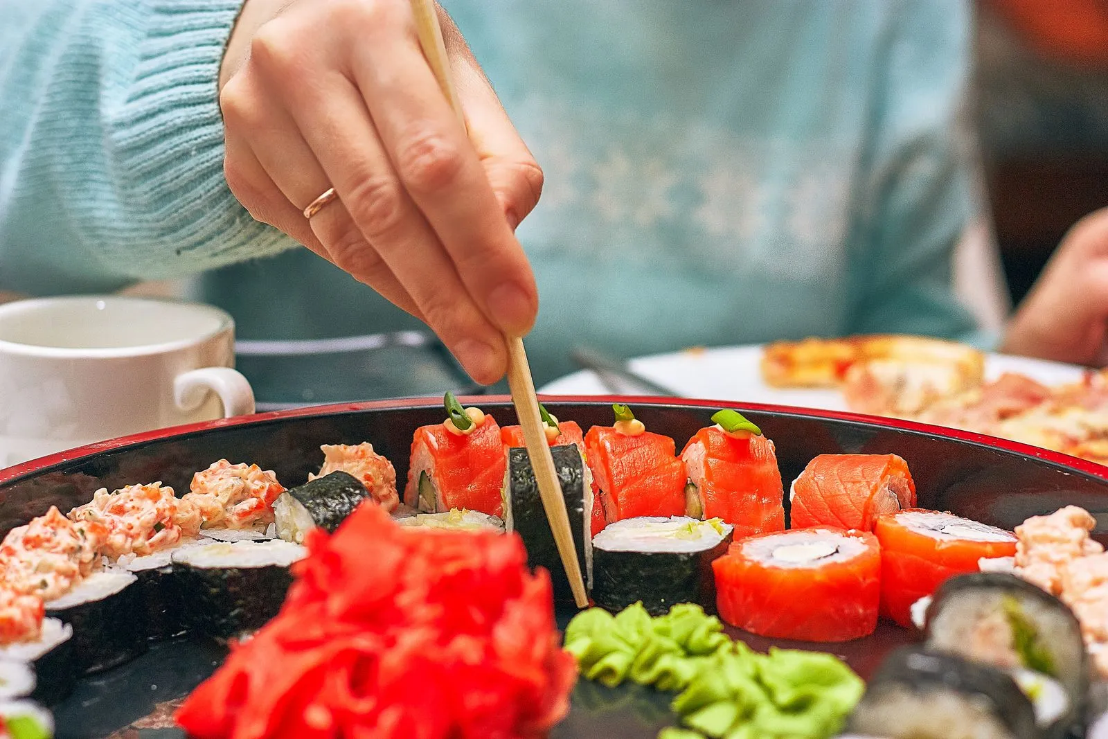 A hand skillfully picks sushi from a platter using chopsticks. Vibrant and delicious.